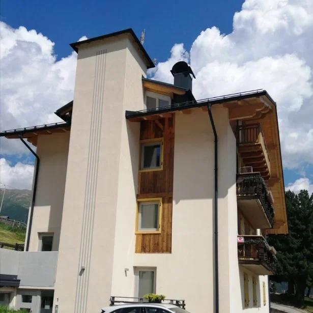 A multi-story mountain building with balconies and wood accents is photographed against a blue sky.